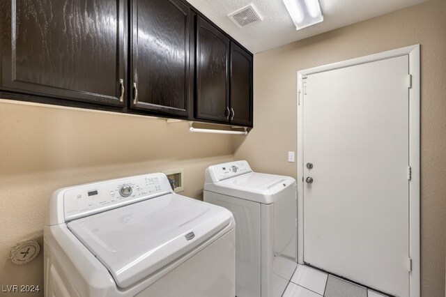 washroom with cabinets, light tile patterned floors, a textured ceiling, and washer and clothes dryer