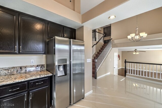 kitchen featuring pendant lighting, ceiling fan with notable chandelier, stainless steel fridge, light stone countertops, and light tile patterned flooring