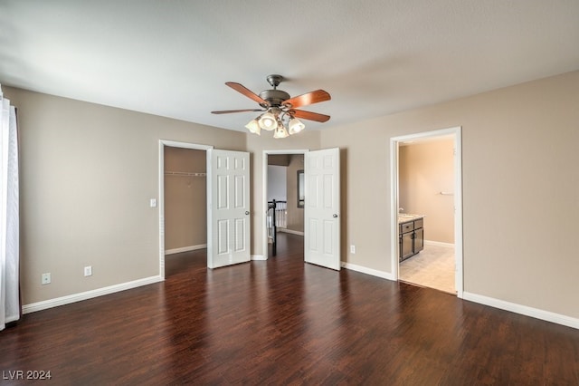 unfurnished bedroom featuring a walk in closet, ensuite bathroom, ceiling fan, dark hardwood / wood-style floors, and a closet