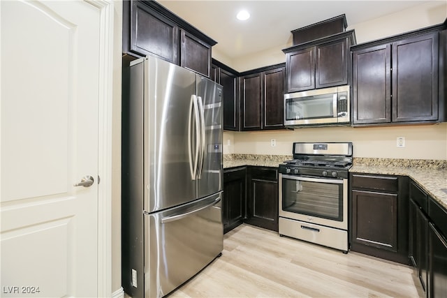 kitchen with light stone counters, light wood-type flooring, dark brown cabinetry, and appliances with stainless steel finishes