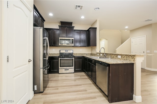 kitchen with kitchen peninsula, appliances with stainless steel finishes, light stone countertops, sink, and light hardwood / wood-style floors