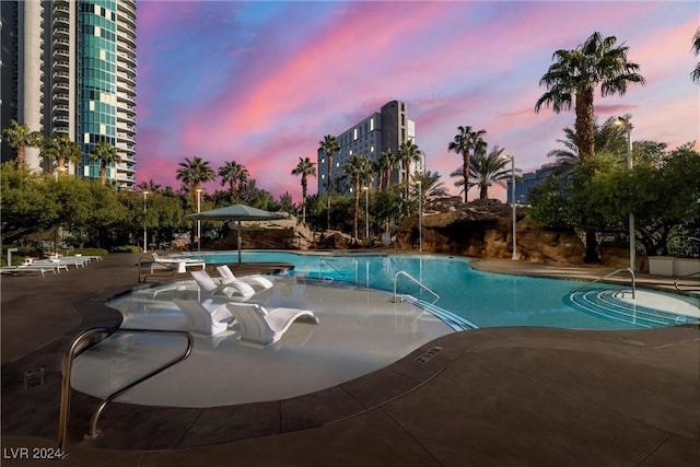 pool at dusk featuring a patio and a community pool