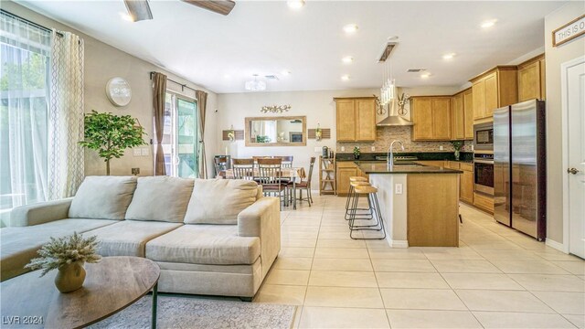 kitchen featuring tasteful backsplash, wall chimney exhaust hood, stainless steel appliances, a center island with sink, and hanging light fixtures