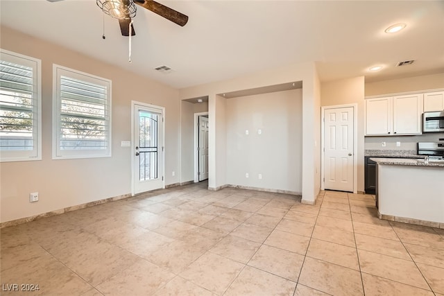 kitchen with white cabinetry, ceiling fan, light stone countertops, stove, and light tile patterned floors