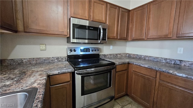 kitchen featuring dark stone countertops, light tile patterned floors, and stainless steel appliances