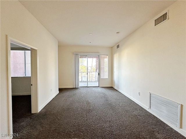 empty room featuring dark carpet, visible vents, and baseboards