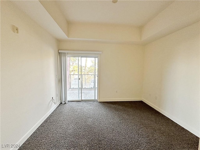 unfurnished room with dark colored carpet, a raised ceiling, and baseboards