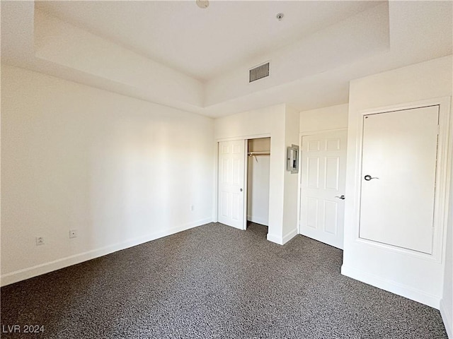 unfurnished bedroom featuring baseboards, visible vents, a raised ceiling, dark carpet, and a closet