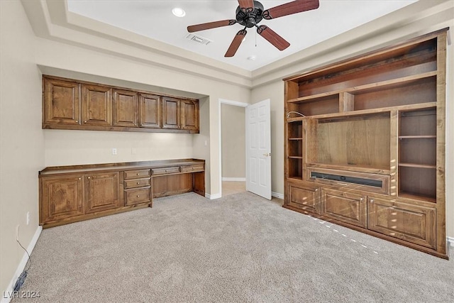 unfurnished office featuring visible vents, baseboards, built in desk, a ceiling fan, and light carpet