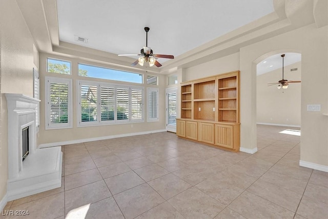 unfurnished living room with a raised ceiling, a glass covered fireplace, a ceiling fan, and visible vents