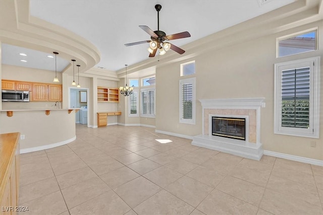 unfurnished living room featuring light tile patterned floors, baseboards, a raised ceiling, ceiling fan with notable chandelier, and a premium fireplace