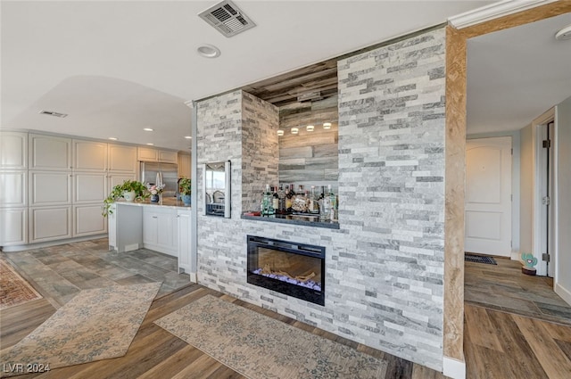 bar featuring stainless steel built in refrigerator, a stone fireplace, and wood-type flooring