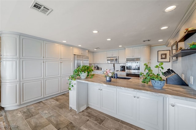 kitchen featuring kitchen peninsula, ornamental molding, stainless steel appliances, sink, and white cabinetry