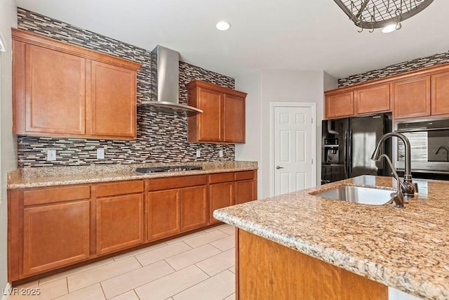 kitchen featuring wall chimney range hood, sink, black fridge, decorative backsplash, and stainless steel gas stovetop