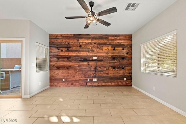 unfurnished living room with ceiling fan, light tile patterned floors, and wood walls