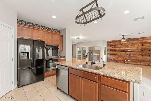 kitchen with wood walls, an island with sink, sink, ceiling fan, and stainless steel appliances