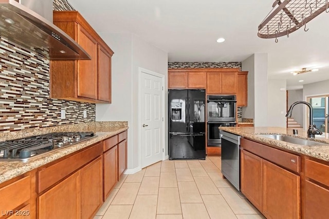 kitchen with sink, wall chimney range hood, stainless steel appliances, light stone countertops, and backsplash