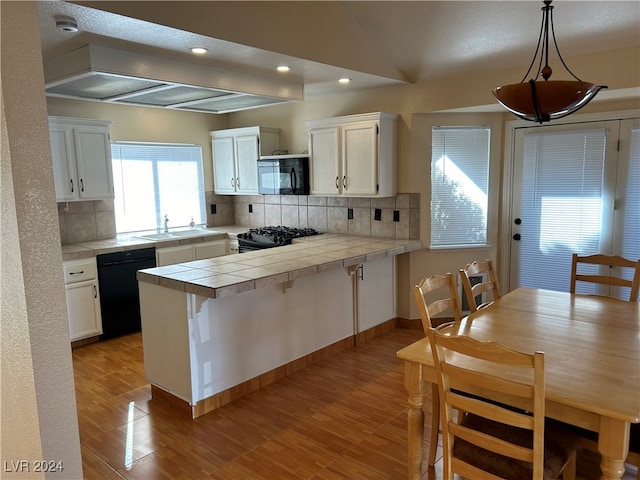 kitchen with kitchen peninsula, white cabinets, black appliances, and decorative light fixtures