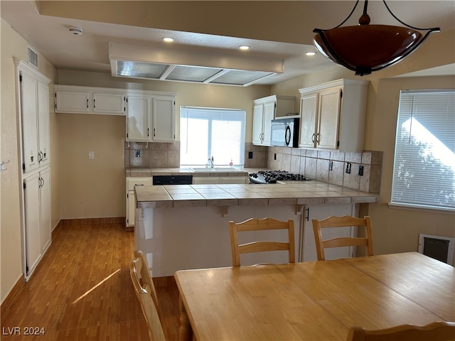 kitchen with white cabinetry, tile counters, pendant lighting, and light wood-type flooring