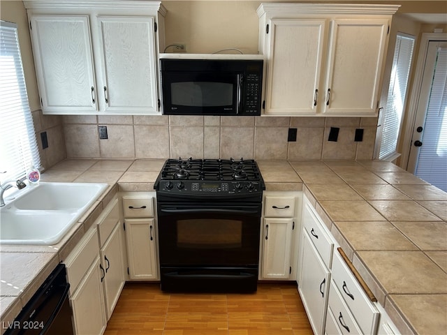 kitchen with tile counters, sink, tasteful backsplash, black appliances, and light wood-type flooring