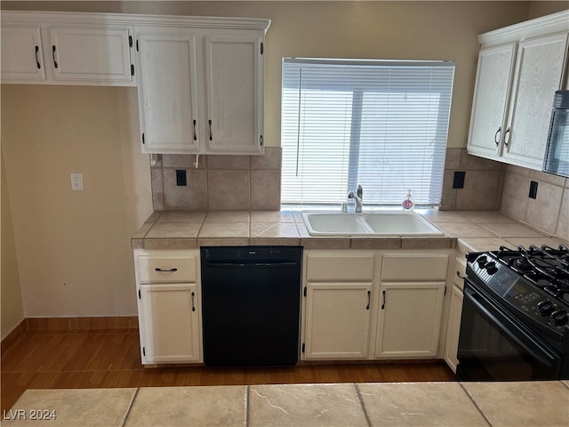 kitchen with tile countertops, white cabinets, black appliances, sink, and tasteful backsplash