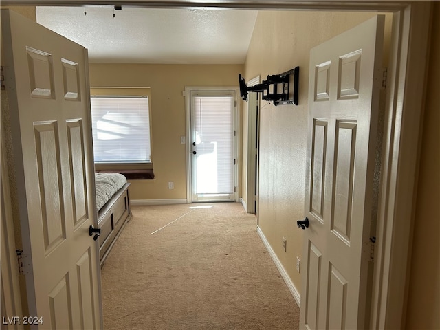 hall with a textured ceiling and light colored carpet