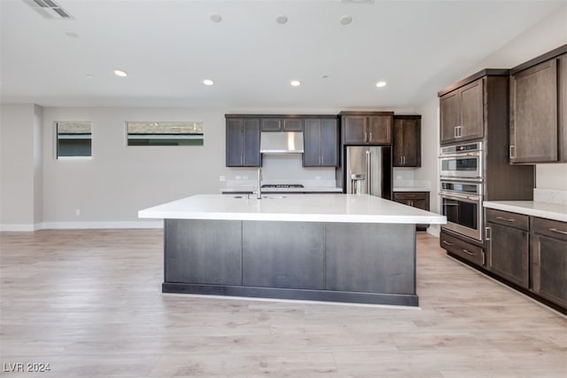 kitchen with dark brown cabinetry, sink, appliances with stainless steel finishes, an island with sink, and light hardwood / wood-style floors