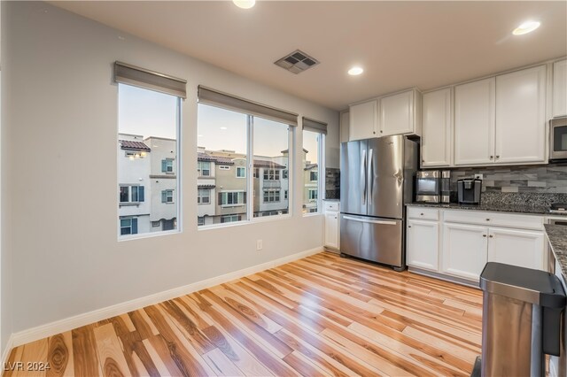 kitchen featuring stainless steel appliances, light hardwood / wood-style flooring, backsplash, dark stone counters, and white cabinets