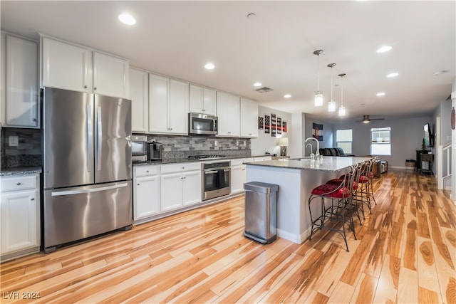 kitchen featuring white cabinets, light wood-type flooring, an island with sink, appliances with stainless steel finishes, and a breakfast bar area