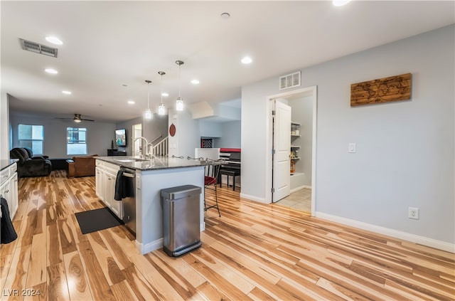 kitchen featuring pendant lighting, a kitchen island with sink, white cabinets, a kitchen breakfast bar, and light hardwood / wood-style flooring