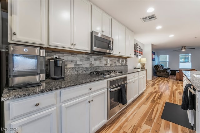 kitchen with dark stone countertops, white cabinetry, stainless steel appliances, and light hardwood / wood-style floors