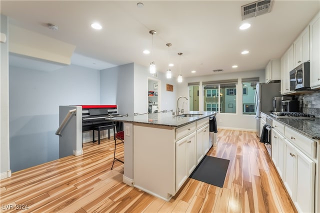 kitchen featuring dark stone counters, a center island with sink, stainless steel appliances, and sink