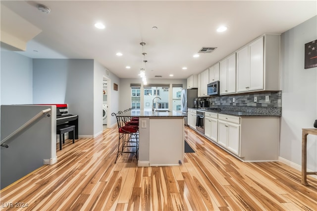 kitchen featuring pendant lighting, stainless steel appliances, a center island with sink, and light hardwood / wood-style floors