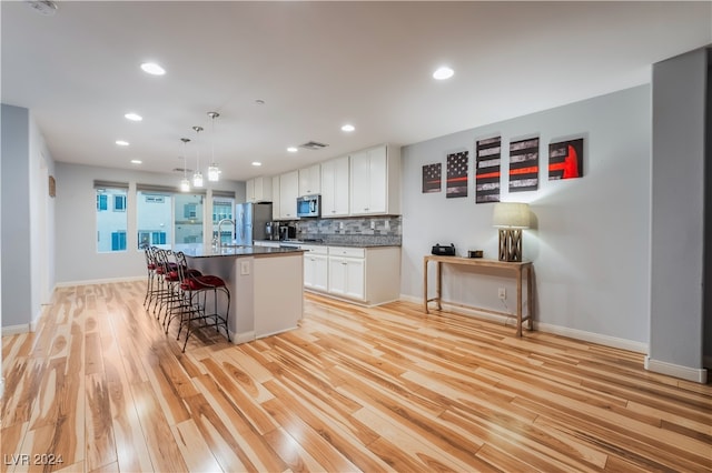 kitchen with appliances with stainless steel finishes, light wood-type flooring, a breakfast bar, a center island with sink, and white cabinets