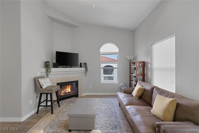 living room with a tiled fireplace, light hardwood / wood-style flooring, and high vaulted ceiling