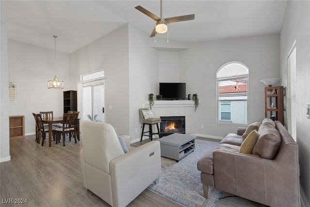 living room featuring a tiled fireplace, ceiling fan, a towering ceiling, and light wood-type flooring