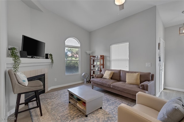 living room featuring a tile fireplace, ceiling fan, high vaulted ceiling, and wood-type flooring