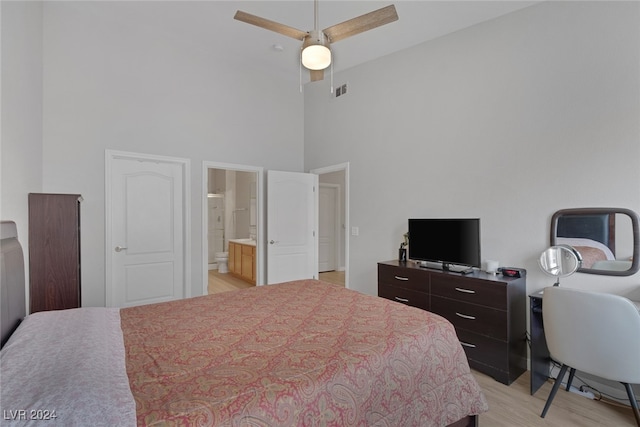 bedroom featuring ceiling fan, light hardwood / wood-style floors, a high ceiling, and connected bathroom