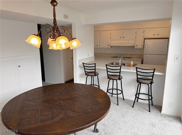 kitchen with cream cabinets, white refrigerator, light colored carpet, and a notable chandelier