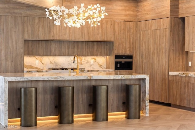 kitchen featuring decorative light fixtures, light parquet flooring, wooden walls, wall oven, and light stone counters