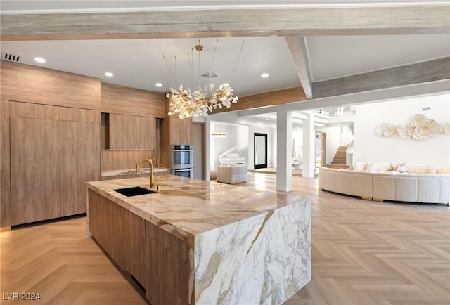 kitchen with a large island with sink, light parquet flooring, sink, light stone counters, and beam ceiling