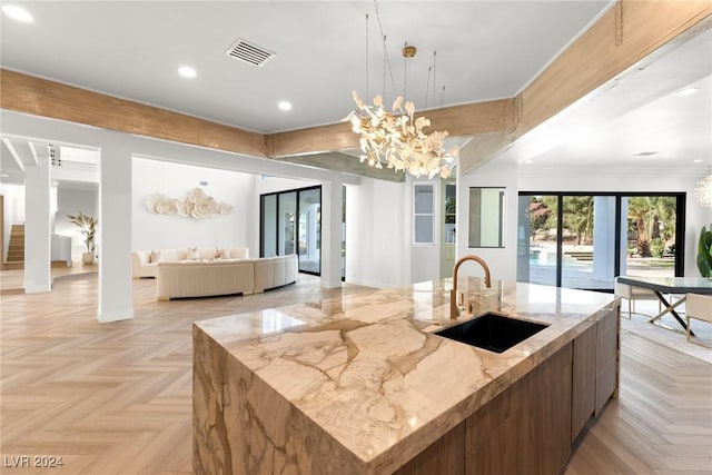 kitchen with sink, pendant lighting, light stone counters, a large island with sink, and light parquet flooring