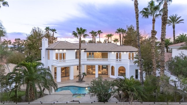 back house at dusk featuring a fenced in pool, a patio, and a balcony