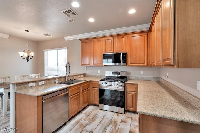 kitchen featuring sink, hanging light fixtures, stainless steel appliances, light stone counters, and kitchen peninsula