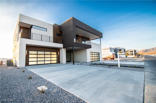 contemporary home with a balcony, central AC unit, an attached garage, concrete driveway, and stucco siding