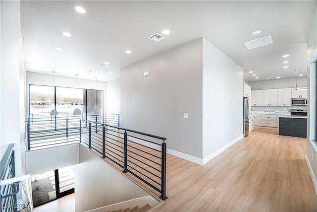 corridor with an upstairs landing, light wood-type flooring, baseboards, visible vents, and recessed lighting