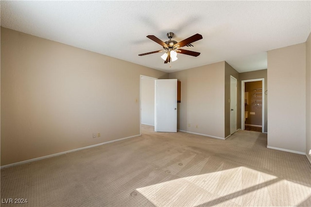 unfurnished bedroom with a spacious closet, light colored carpet, a closet, and ceiling fan