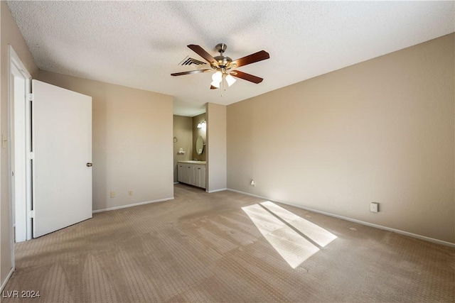 unfurnished bedroom featuring light carpet, a textured ceiling, ceiling fan, and ensuite bath