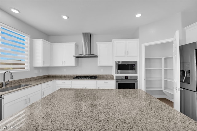 kitchen featuring wall chimney exhaust hood, white cabinetry, sink, and appliances with stainless steel finishes