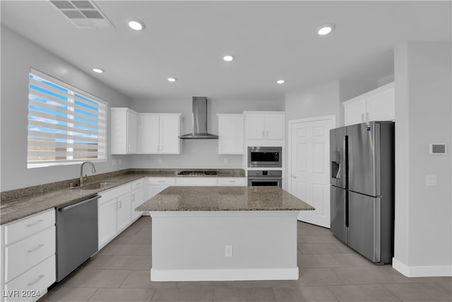 kitchen featuring appliances with stainless steel finishes, a center island, wall chimney exhaust hood, and dark stone countertops